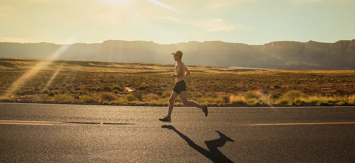 A shirtless man running on the road in the sun