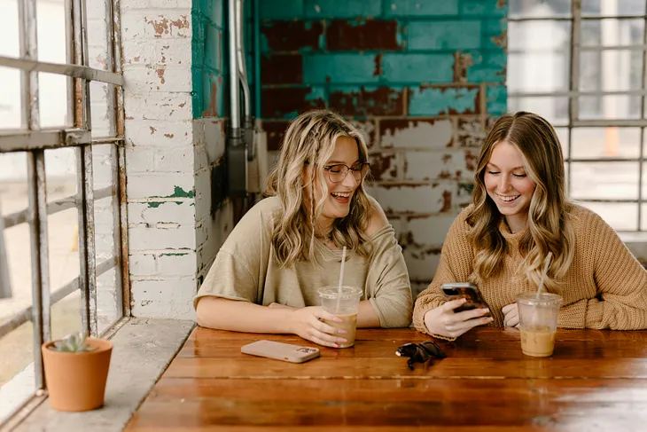 Two girls discussing something on a phone and enjoying a drink