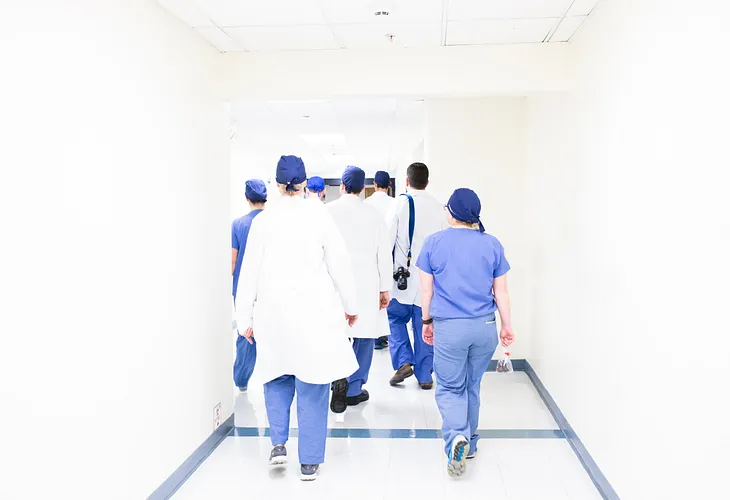 A group of white-jacket medical staff walk away with their backs turned on the reader.