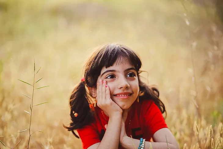 A cute little girl smiles brightly, her red shirt and big smile telling.