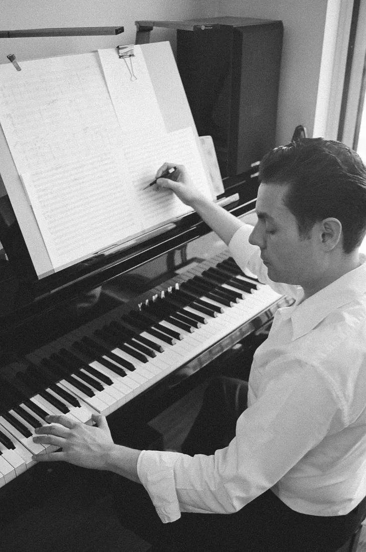 Black and white looking down as man writes at piano