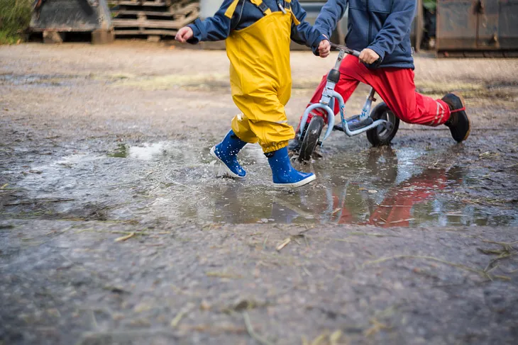 Two children, one jumping in a puddle and one riding a bike through the puddle.