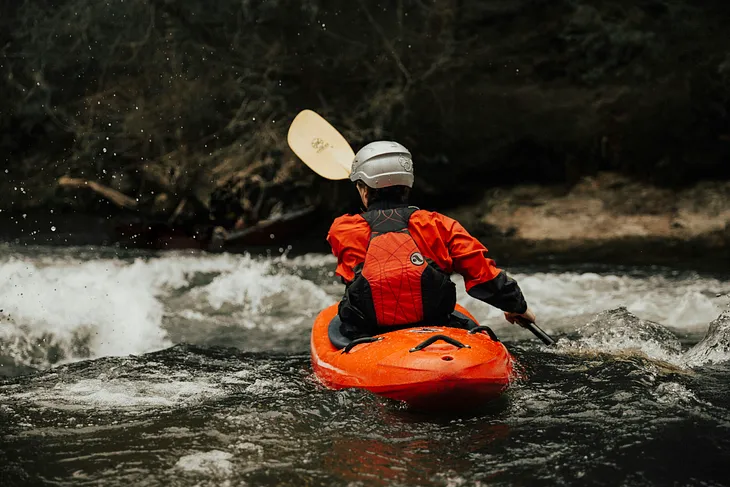 A kayaker wearing a helmet heading into white water.