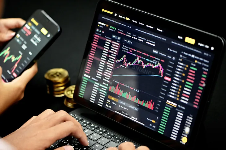Photo shows a small computer screen with a financial chart open. A person’s hands hovers over the keyboard.