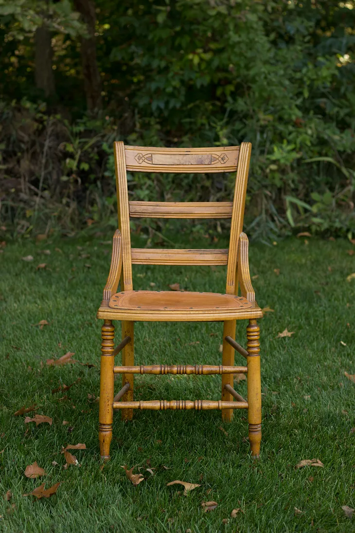 An empty wooden chair sitting on a lawn