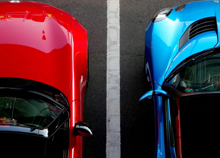 A cropped shot of 2 cars: red in left, blue in right; separated by the lane line.