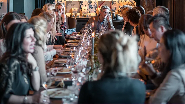 A Modern Dinner Party: Well-dressed, happy-looking people sit around a long dining table, chatting happily.