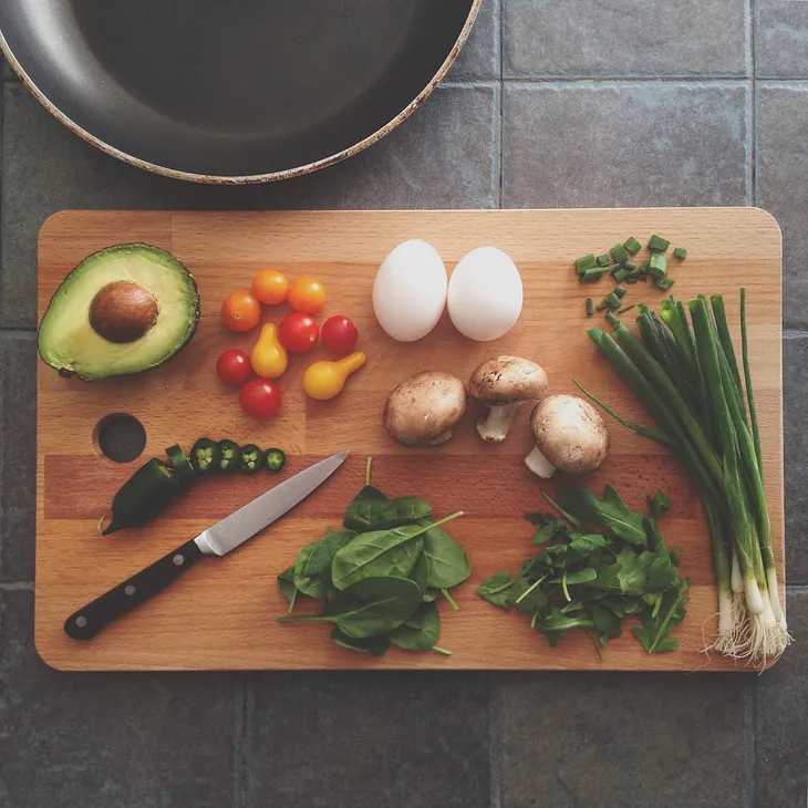 A large cutting board with fresh vegetables and a knife.