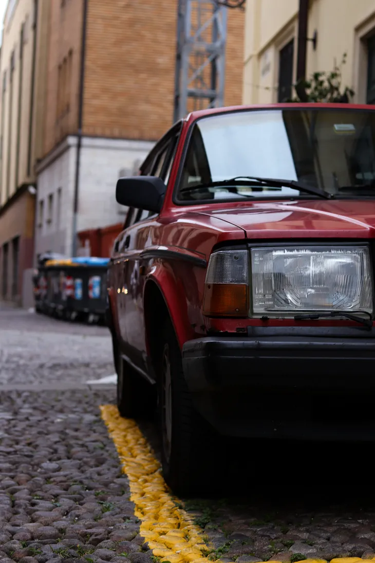 A red car parked too close to the yellow parking line