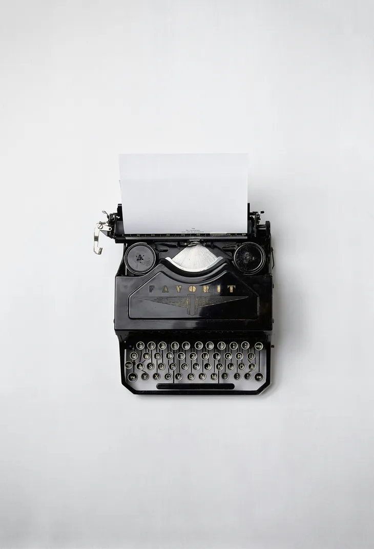Black typewriter with a sheet of paper in it and a few words typed at the bottom of the page. White background