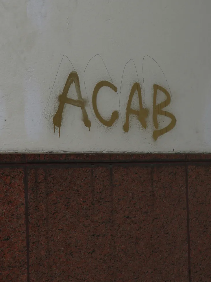 The letters “A C A B” spray-painted on a wall.