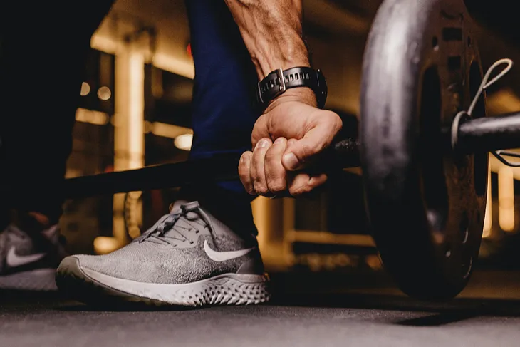 A man wearing blue jeans and grey sneakers holding a barbell close to the floor