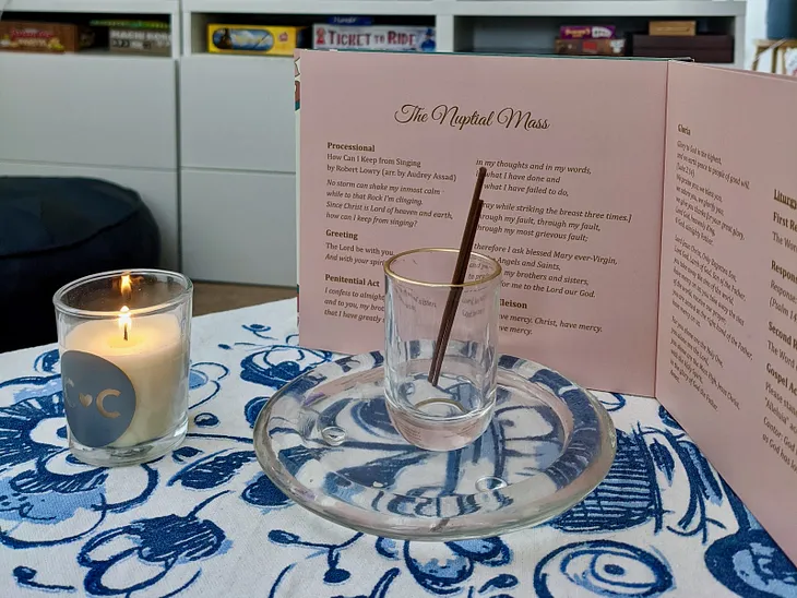 Incense, a candle, and a bound wedding program on a table with a blue and white floral tablecloth.