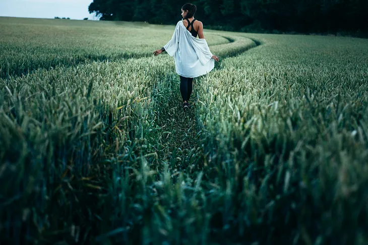 The writer pictures a woman walking through tall grass in an open field.