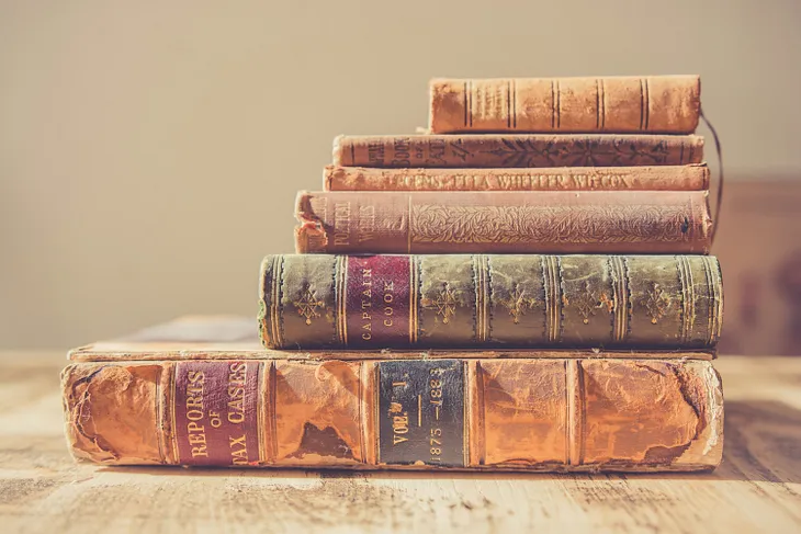 Stack of old, pale books on their sides, longest on bottom, shortest on top.