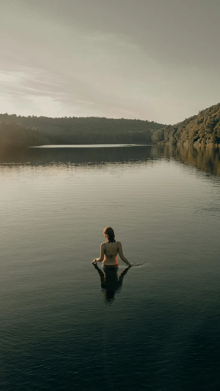 A woman in a bikini walks into a lake.