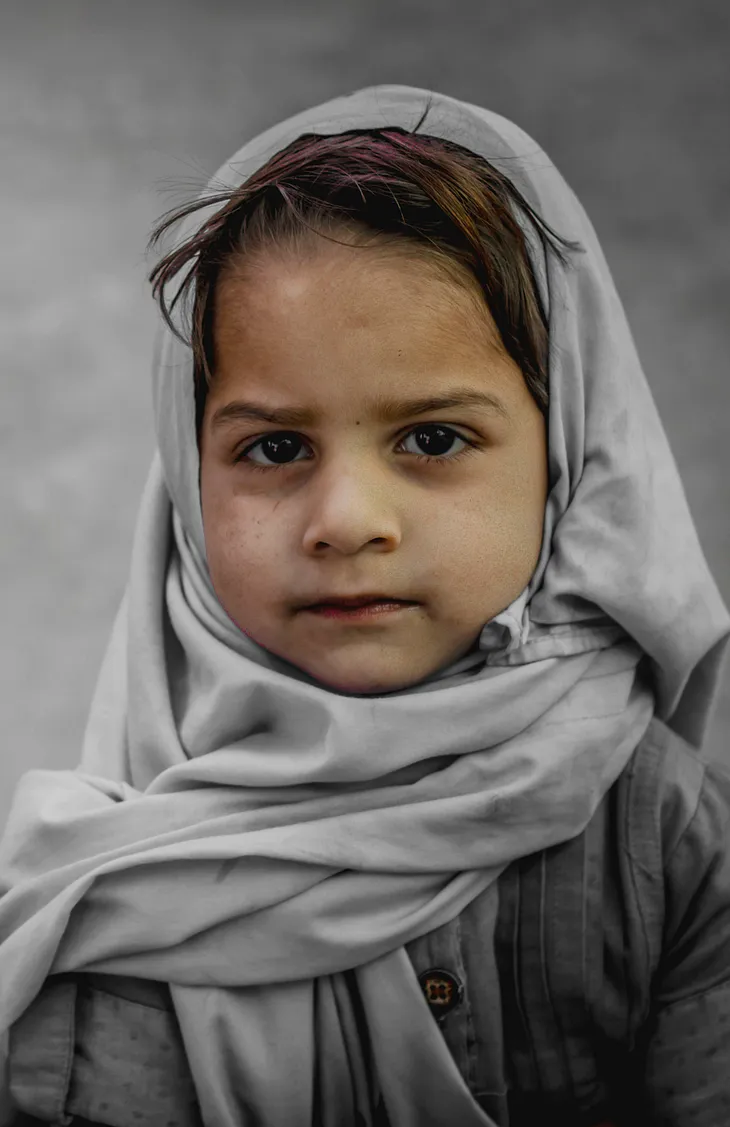 A young girl in a Hijab, looking at nothing in particular and unsure of what may happen.