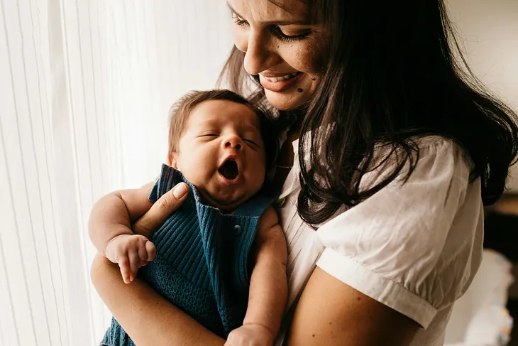 Mom smiling while holding a yawning baby