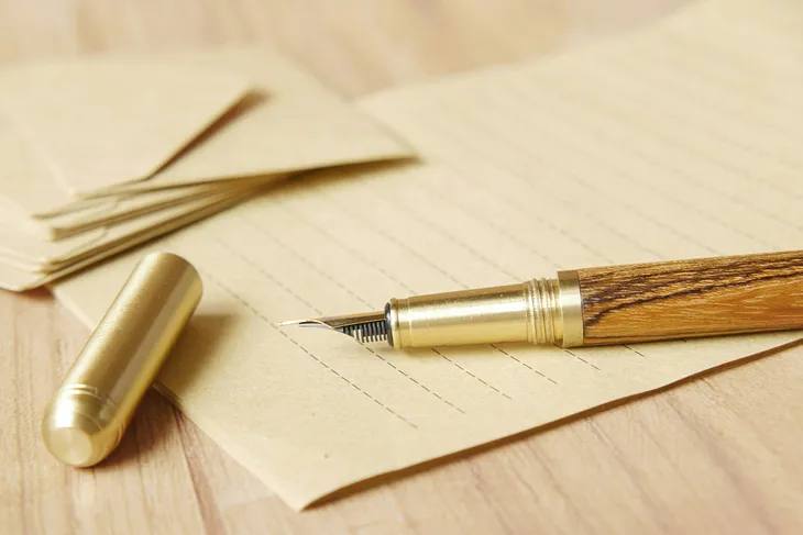 Uncapped brown wooden fountain pen and lined writing paper.