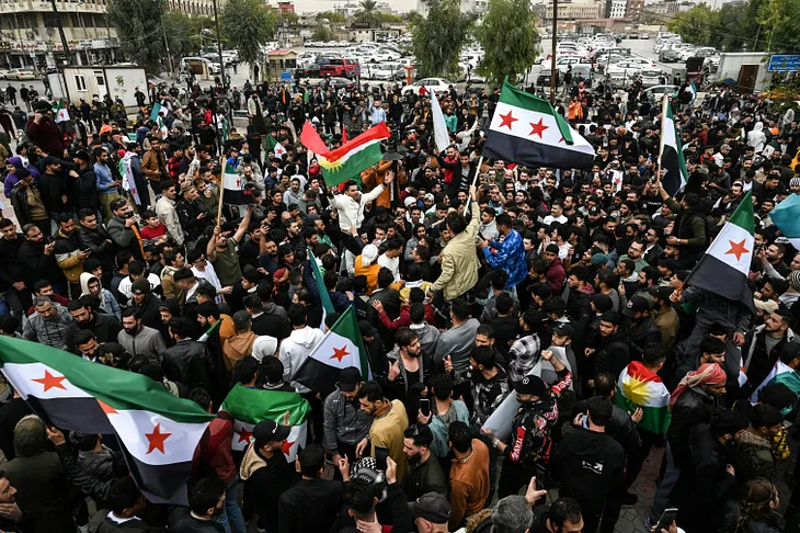 A crowd of men celebrate in a public square while saving flags of the Syrian opposition.