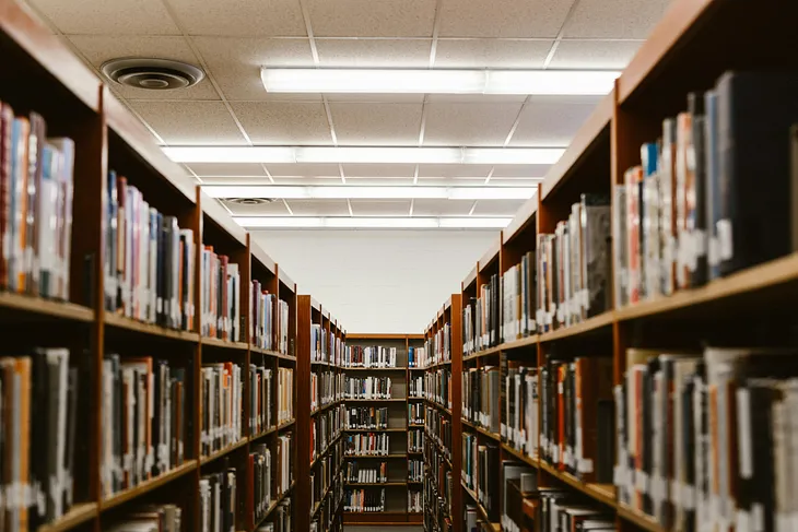 An aisle in a library, books on either side in shelves.