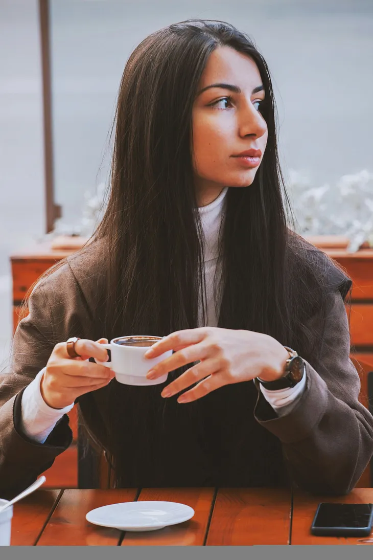 A woman in a corporate suit drinking coffee while looking at her far left side