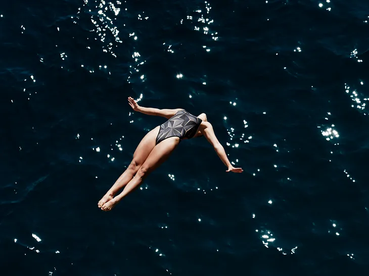 A cliff diver free-falling backwards into the ocean.