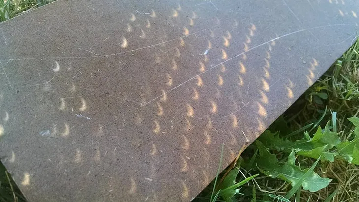 Sidewalk with shadows of partial eclipse filtered through tree leaves.