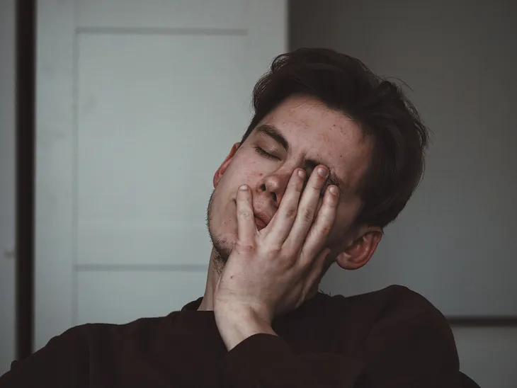 A man, with his hand on his face, looking very tired.