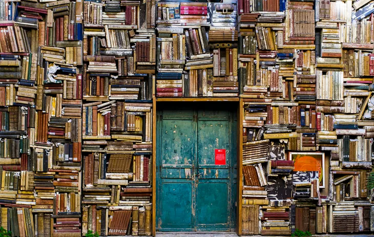 A wall of old book spines with a blue door in the center