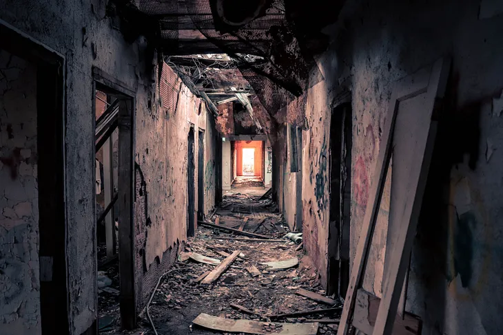 Hallway of an abandoned building with a sunlit doorway at the end