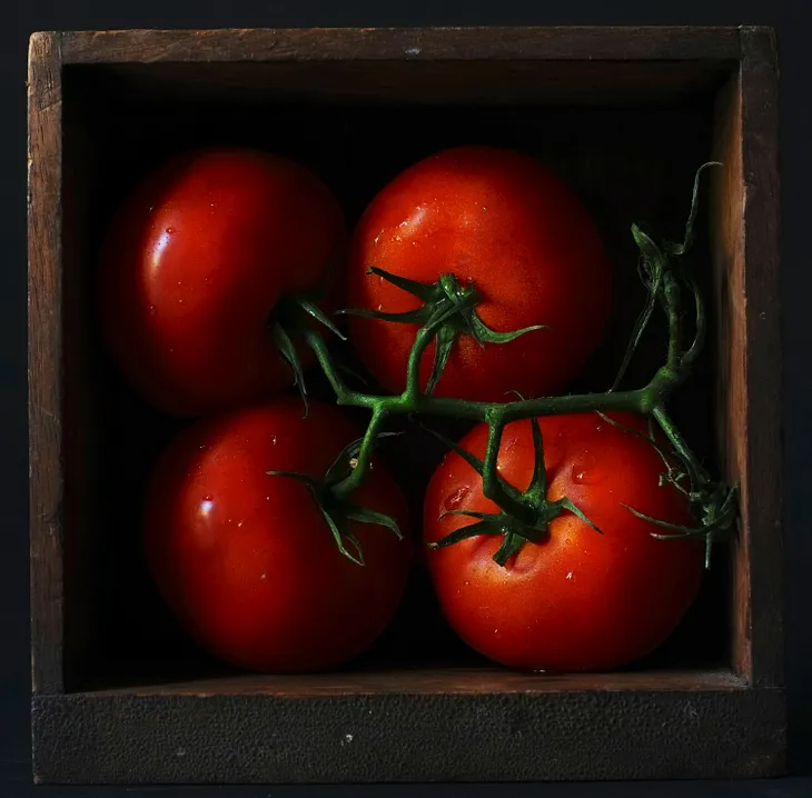 4 deep red tomatoes on the vine in a thin wooden box