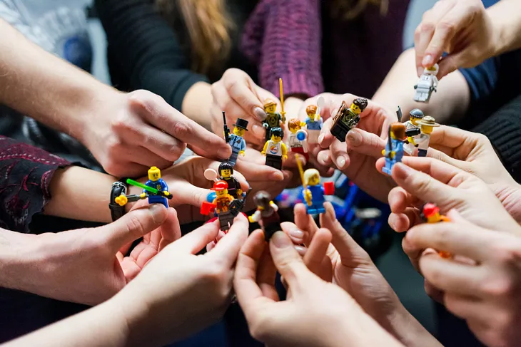 A team is all in with hands in a group holding toy figurines.