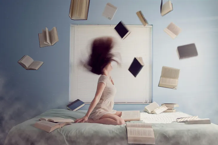 A girl sitting on the bed with books hanging in the air