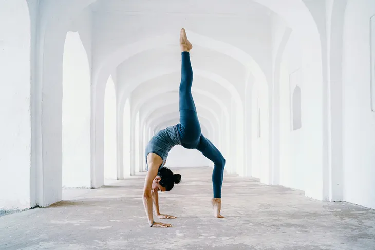 A woman doing a yoga pose in an empty hallway in an all-white building