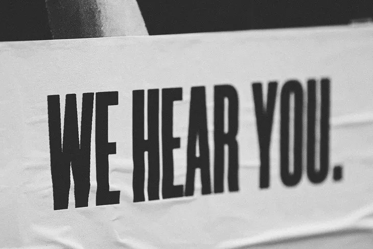 White poster with the words “We hear you” written in black.