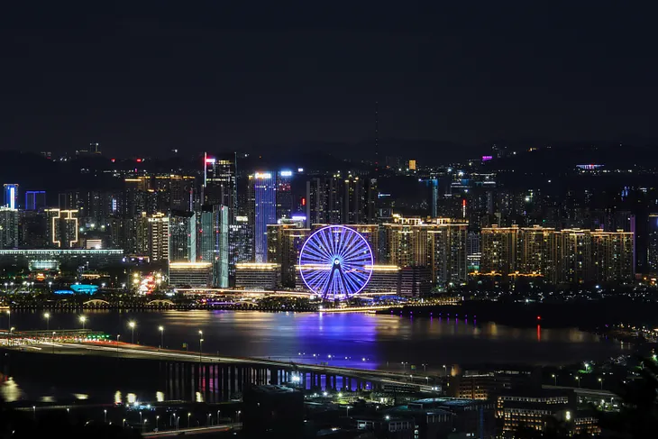 The skyline of Shenzhen that prominently features a neon purple Ferris wheel casting a throw of light over water