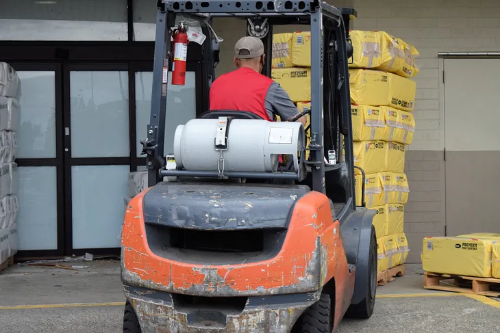 Forklift operator seen from behind operating an orange forklift.