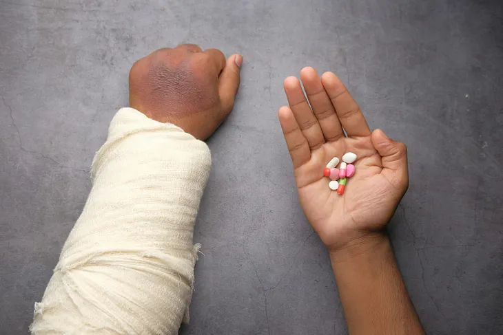 An image of a broken arm and a handful of pills.