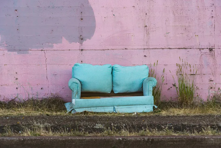 An old, broken blue sofa in front of a pink wall