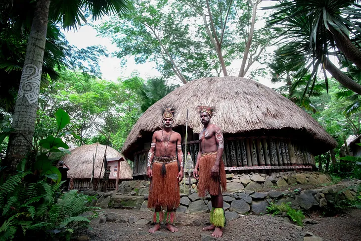 Two Village Men Standing before a hut in the jungle.