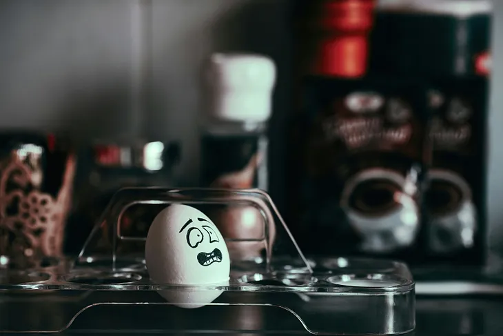 A white egg sits in a clear plastic tray. It has a face of frustration painted on it.