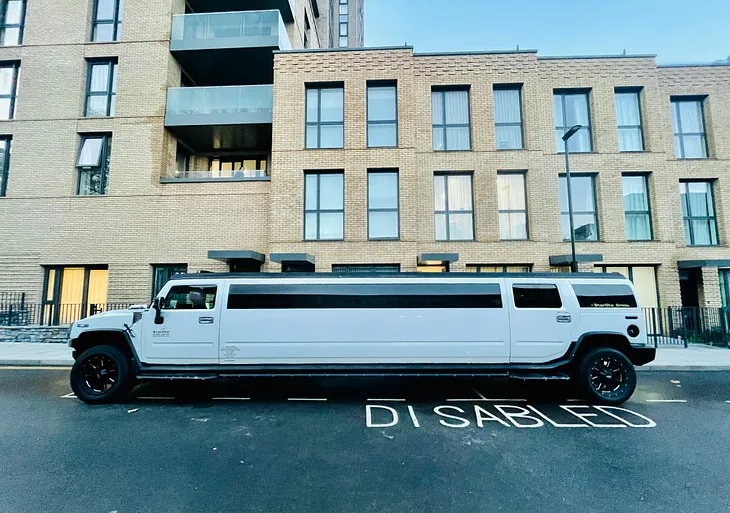 A chunky white party limousine parked on a disabled parking spot.