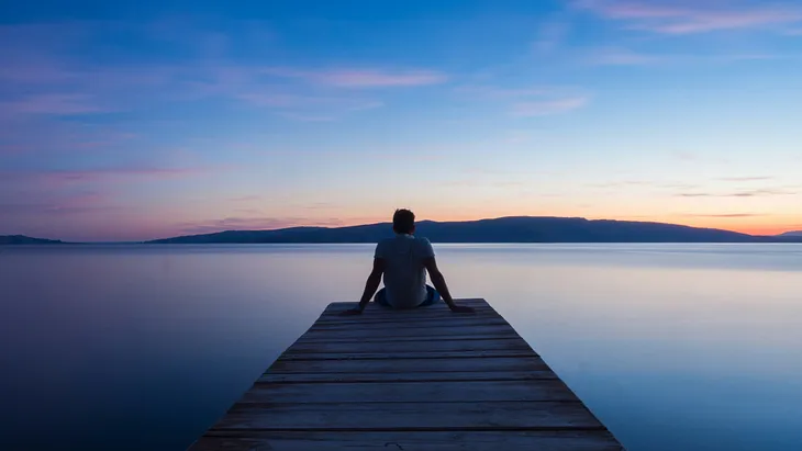 Image describe a person sitting on the middle bridge of riverbed.