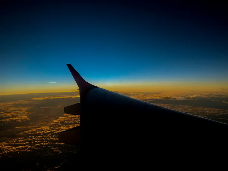 Airplane look out over the left wing with sunset and clouds in the background