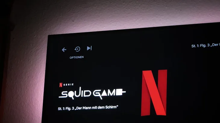 This picture shows the screen on Netflix where it shows the text ‘Squid Game’ alongside the Netflix ’N’ logo. This is shown on a TV screen which appears to be attached to a wall.