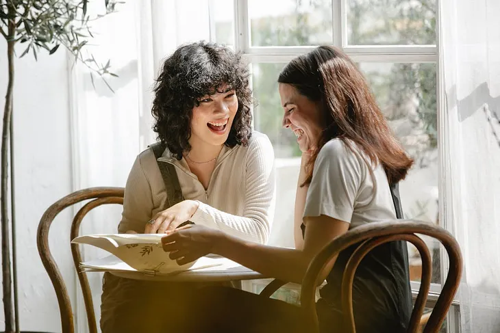 Two women sharing a positive conversation in a bright white room while looking at and discussing a document in front of them