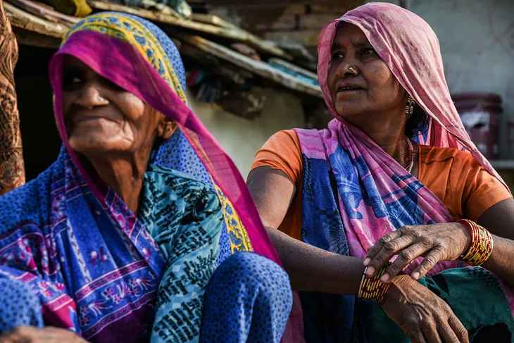 Two Indian women sit outside their huts