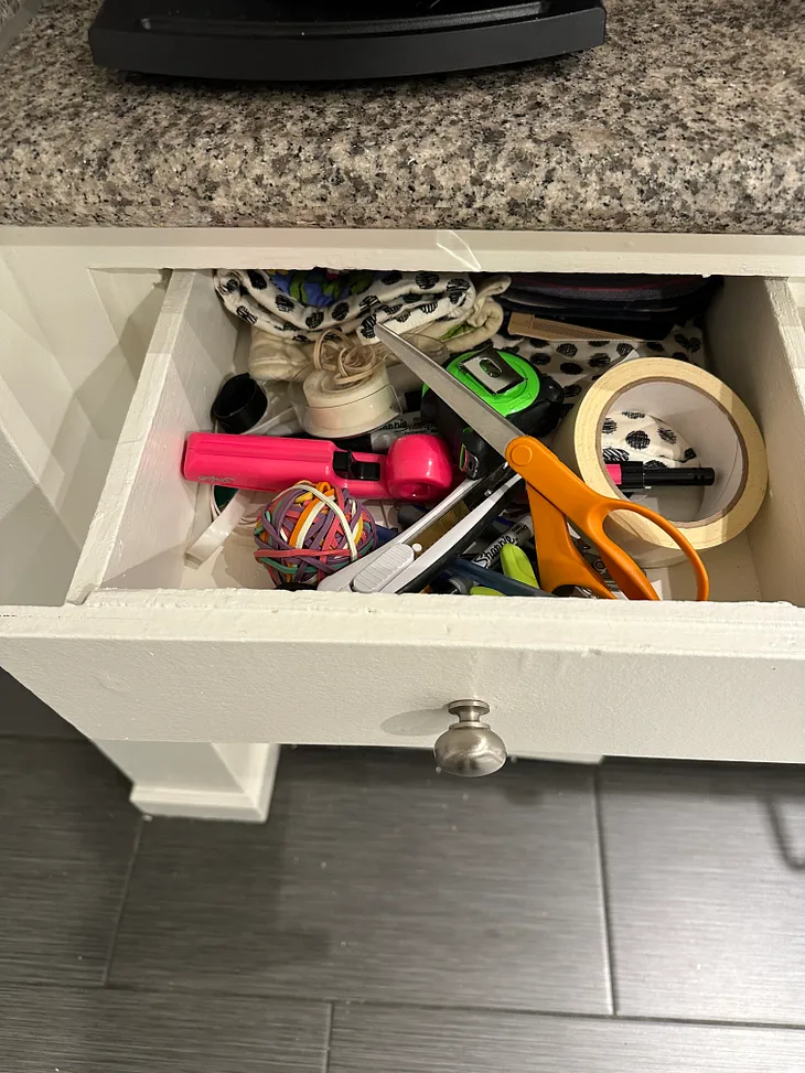 a junk drawer containing, scissors, tape and a rubber band ball amongst other items.