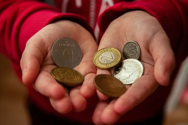 A child’s hands in a red sweater holding 6 coins